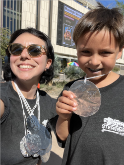 Woman and child pose smiling in the Sun, wearing black t-shirts and tin foil made medallions 
