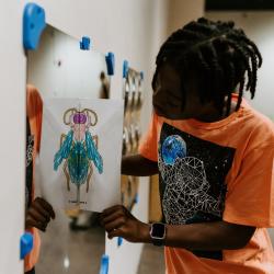 An individual holds up an insect coloring sheet folded in half to a mirror on the wall to create a full image of the insect.