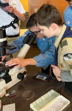 Two individuals bend down to a telescope sitting on a table. One is looking in while the other watches and waits their turn.