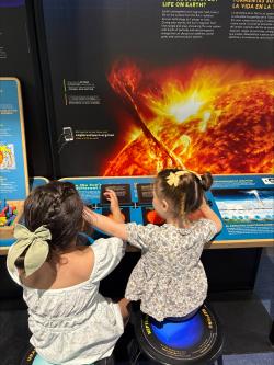Two Youth sit at the We Ask Questions about the Sun component of SEU, they are lifting flaps on the reading rail.