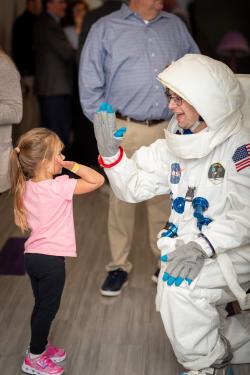 An individual wearing an astronaut suit kneels down to give a young child a high-five.