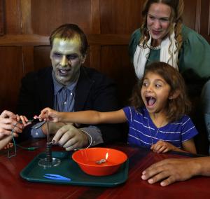 Child with excited facial expression using battery stack activity with adults dressed as Mary Shelley and Frankenstein's monster