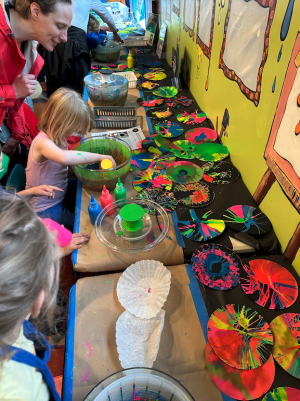 Nebula Spin Art Activity Table with young girl adding paint to spinner while adult watches