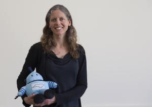 Presenter Headshot - Amy Sayle Smiles Holding Kelvin Stuffy and wearing dark long sleeves 