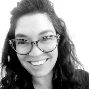 Close up in black and white of a woman smiling and wearing glasses.
