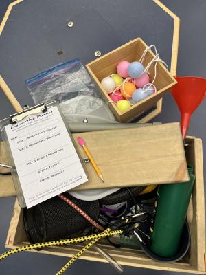 Random resources in wooden bins and plastic bags lay across a black tabletop with a small clipboard with pencil and short form.