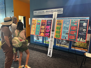 A family views a colorful, large-format radio technology timeline display at a science center exhibit. Ask ChatGPT