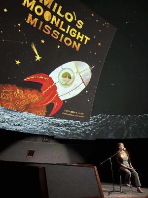 Inside the dome of a planetarium an individual sits on a stool in front of a mic. As they speak, the dome shows the image of a book cover showing a rocket blasting off and the title "Milo's Moonlight Mission."