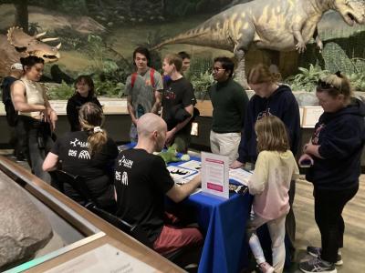 A diverse group of learners view a model of a T-Rex's brain at a table top activity positioned in a dino exhibit.