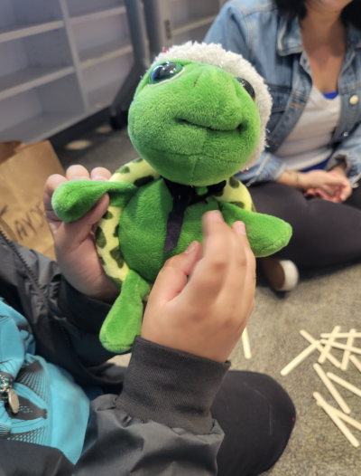 Hands hold a stuffed frog that appears to be wearing a Santa hat.
