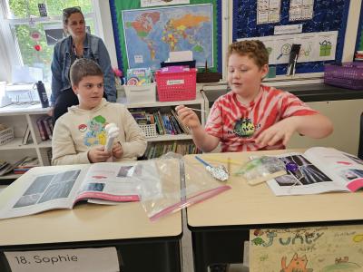 Two youths sit at desks in a classroom, they have booklets open looking at some sort of activity supplies.