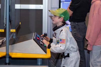 Child in Astronaut Suit Plays at a console with various pushbuttons and switches. 