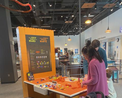 Build a Human Habitat on Mars exhibit with instruction graphics, table top building surface, and guests building with blocks - Table view