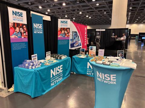 NISE Network exhibit booth with teal tables, banners, and educational materials at a conference.
