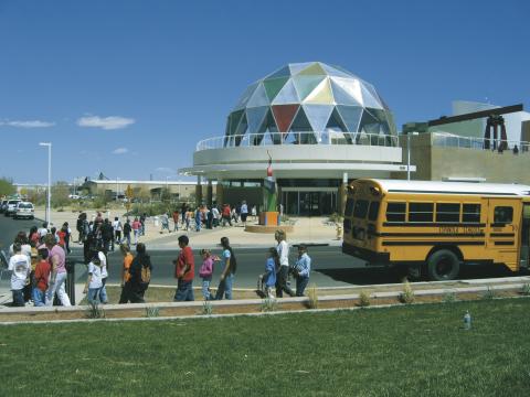 The front of the Explora Museum building, showing the large dome on top the entrance as a school bus drops a group of youth at the door.