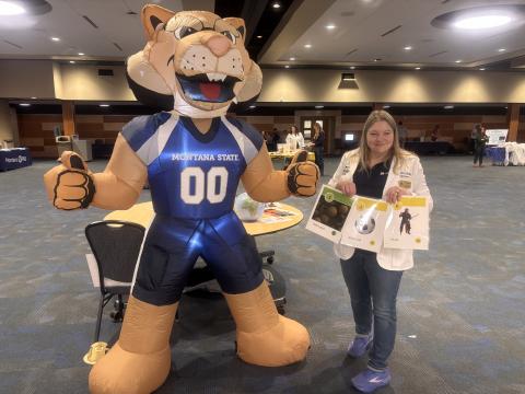 An individual stands next to the Montana State University mascot Bobcat.