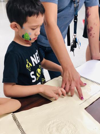 Child looking using his hand to feel textures in a tactile book about Earth and space science