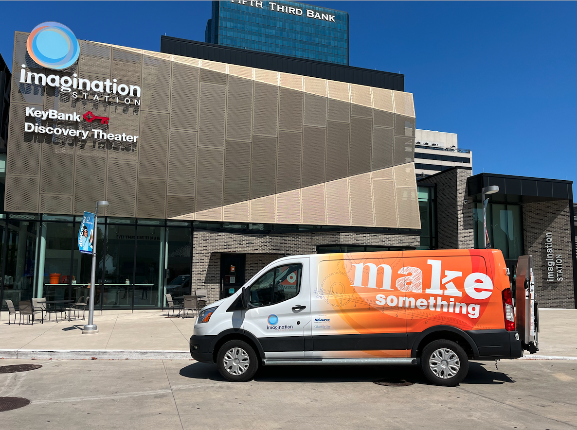 Imagination Station Toledo front of the building on a sunny day with blue skies. A van parked in front that says "Make Something" in white on the orange back side of the van.