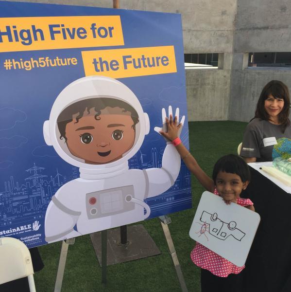 Image of child standing in front of a poster reading "High Five for the Future"