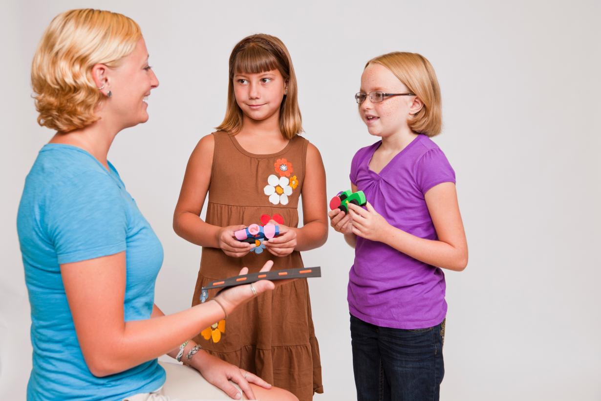 Two girls discuss their ideas for flying cars with toy car props to a facilitator