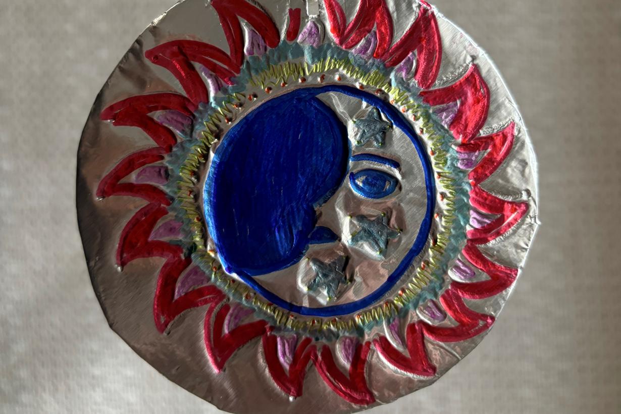 A colorful etching of the sun in tin foil with a string laced through the top in a loop.