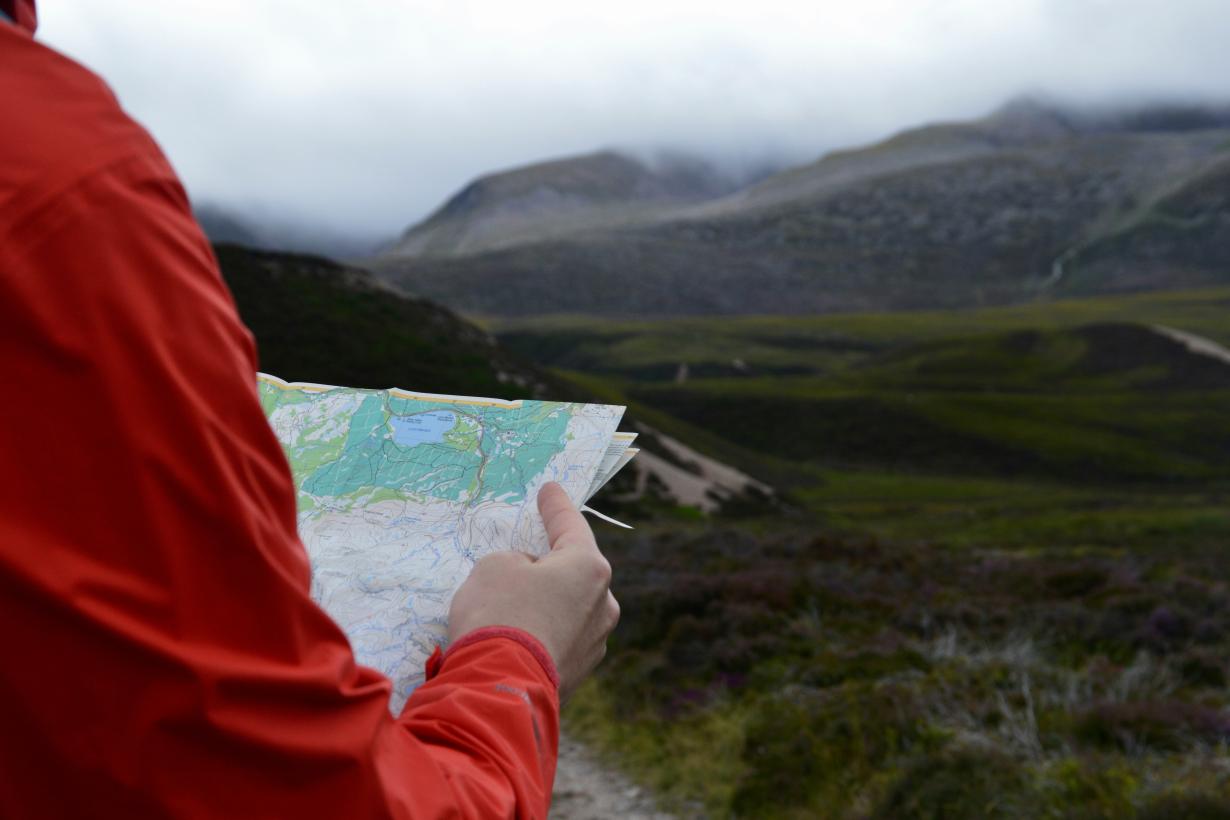Navigating person holding a map looking at mountain clouds 