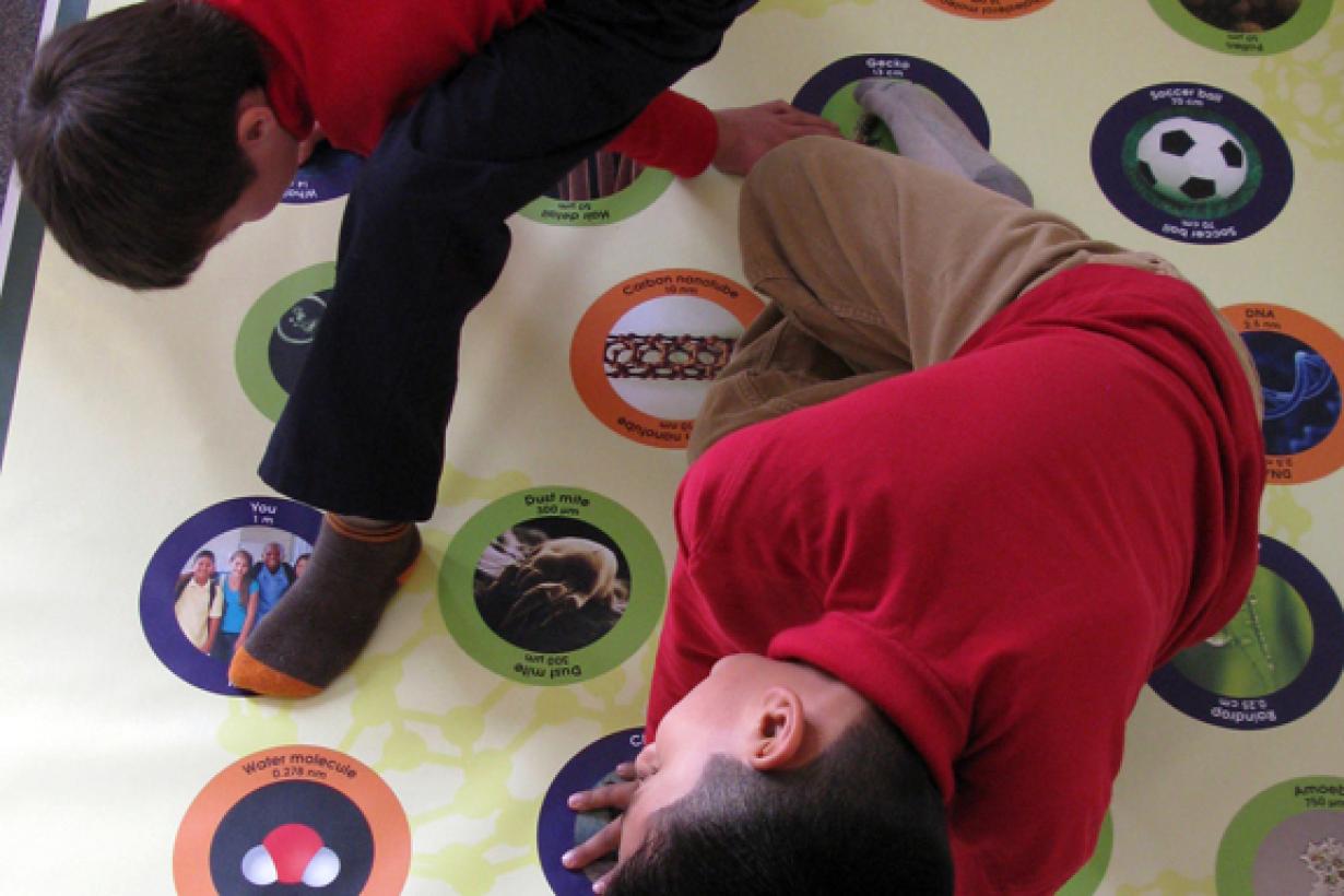 two learners stretch across a large mat that have various icons related to nanotechnology