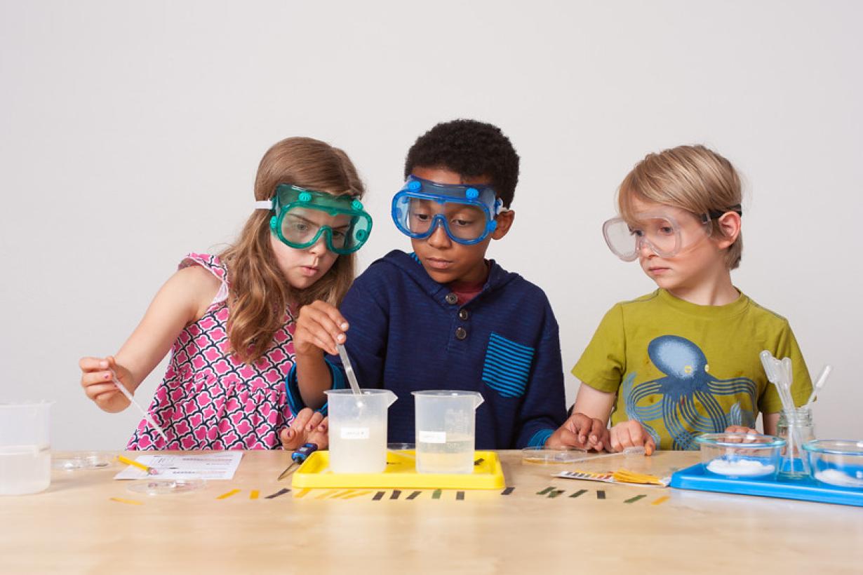 Three children measuring and mixing liquids using pipettes and beakers