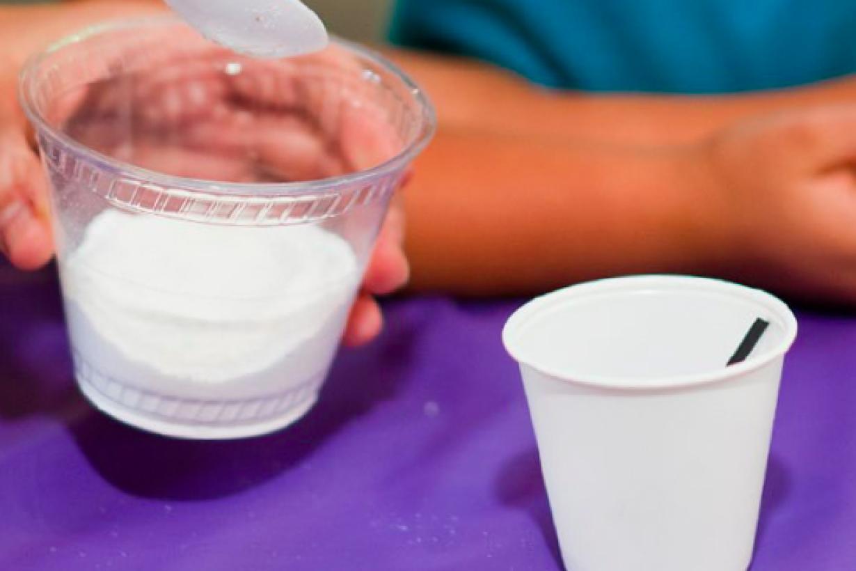 hand spooning white powder material into cup in Exploring Materials - Hydrogel NanoDays activity