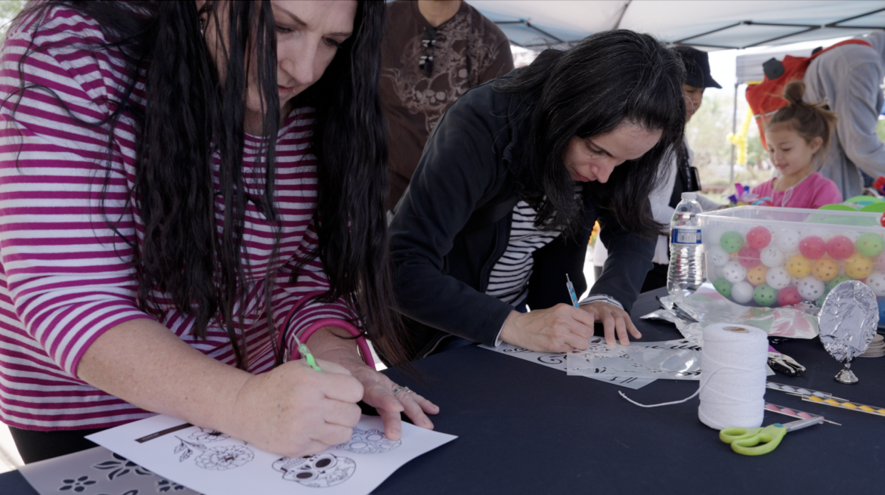 Two adults stand leaning over a table as they draw and trace onto foil.
