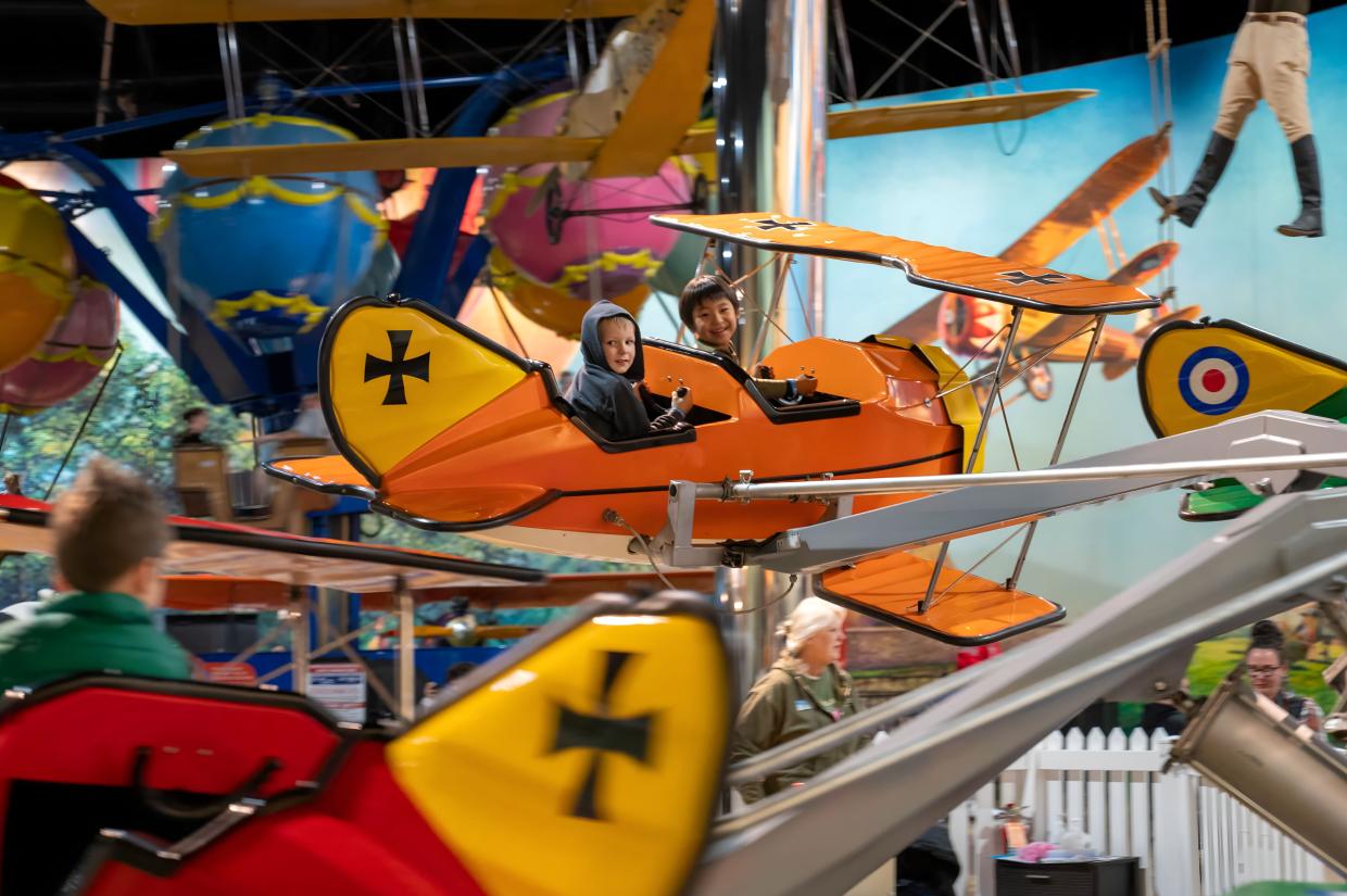 Two children smile while riding on an amusement park style plane ride.