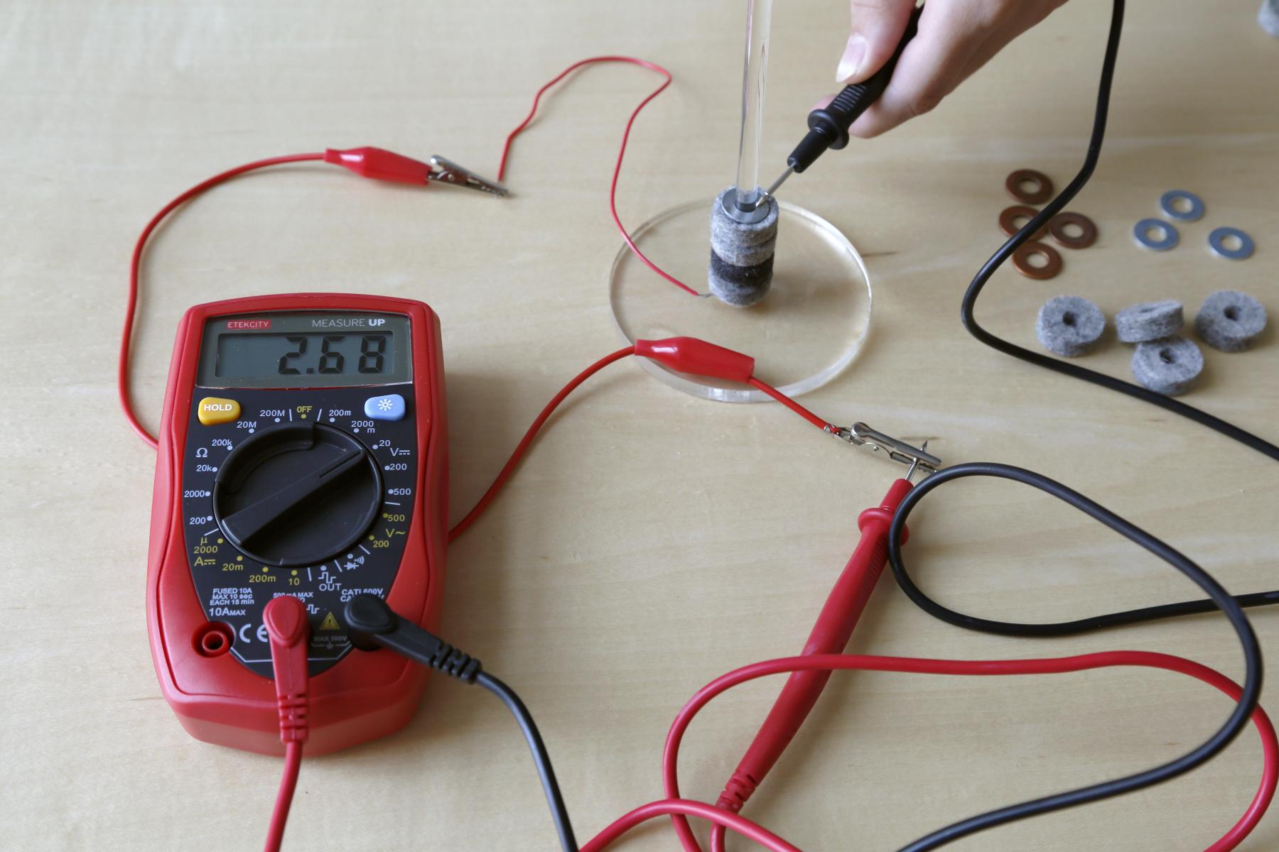 voltaic pile connected to multimeter on table with washers