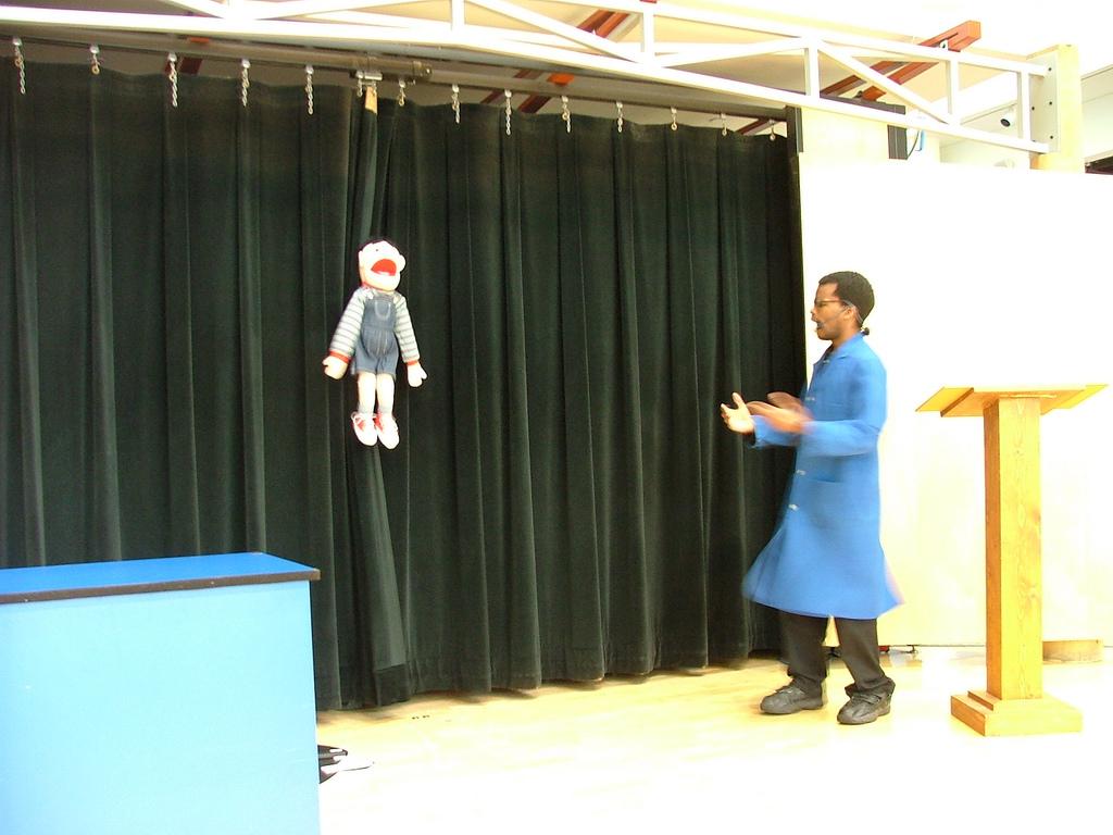 An actor with a blue lab coat on stage with a puppet talking about nano