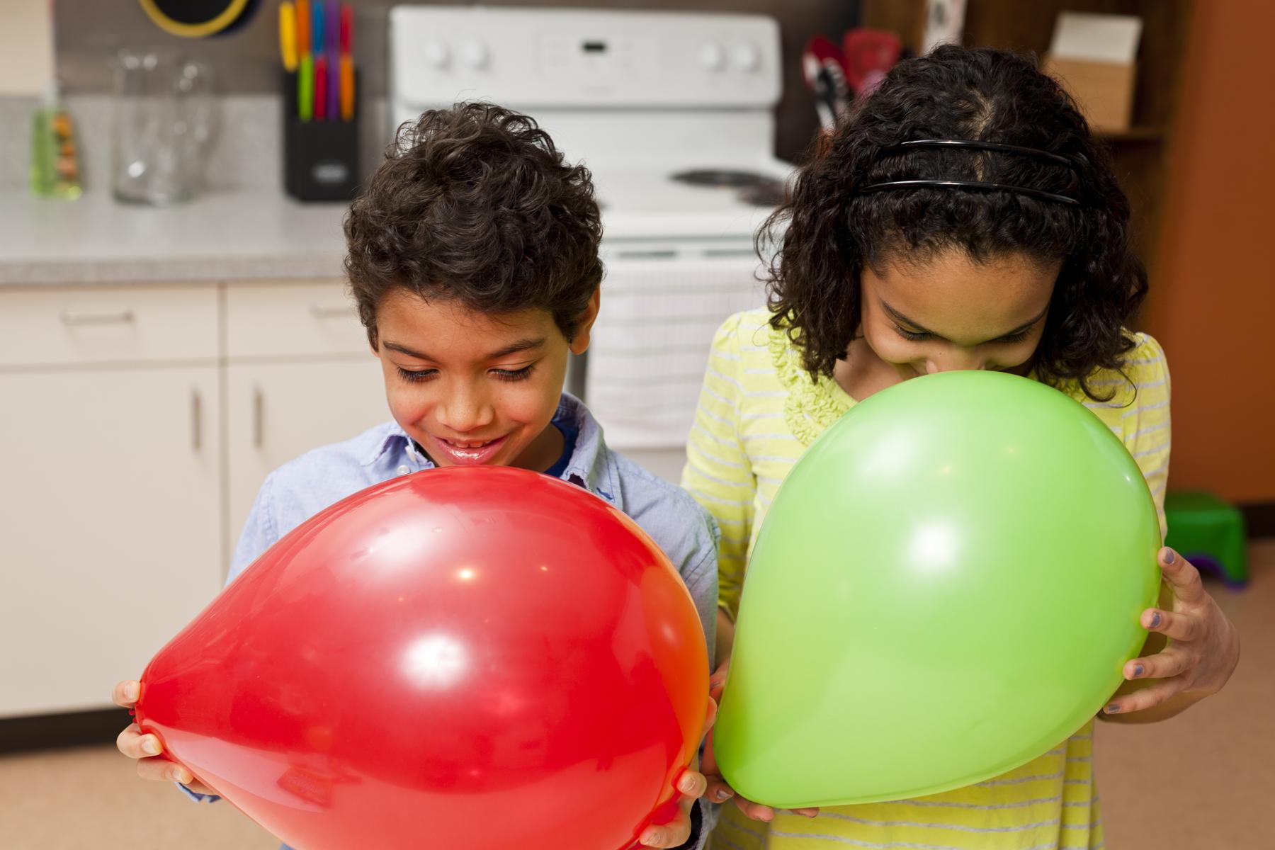 Two learners hold green and red balloons and smell them to identify the hidden scent inside
