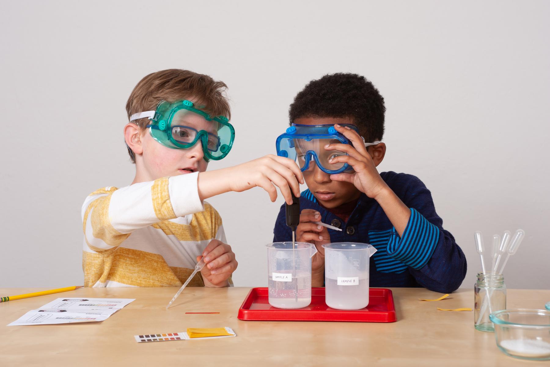 Two learners wearing goggles measure water temperature with a thermometer