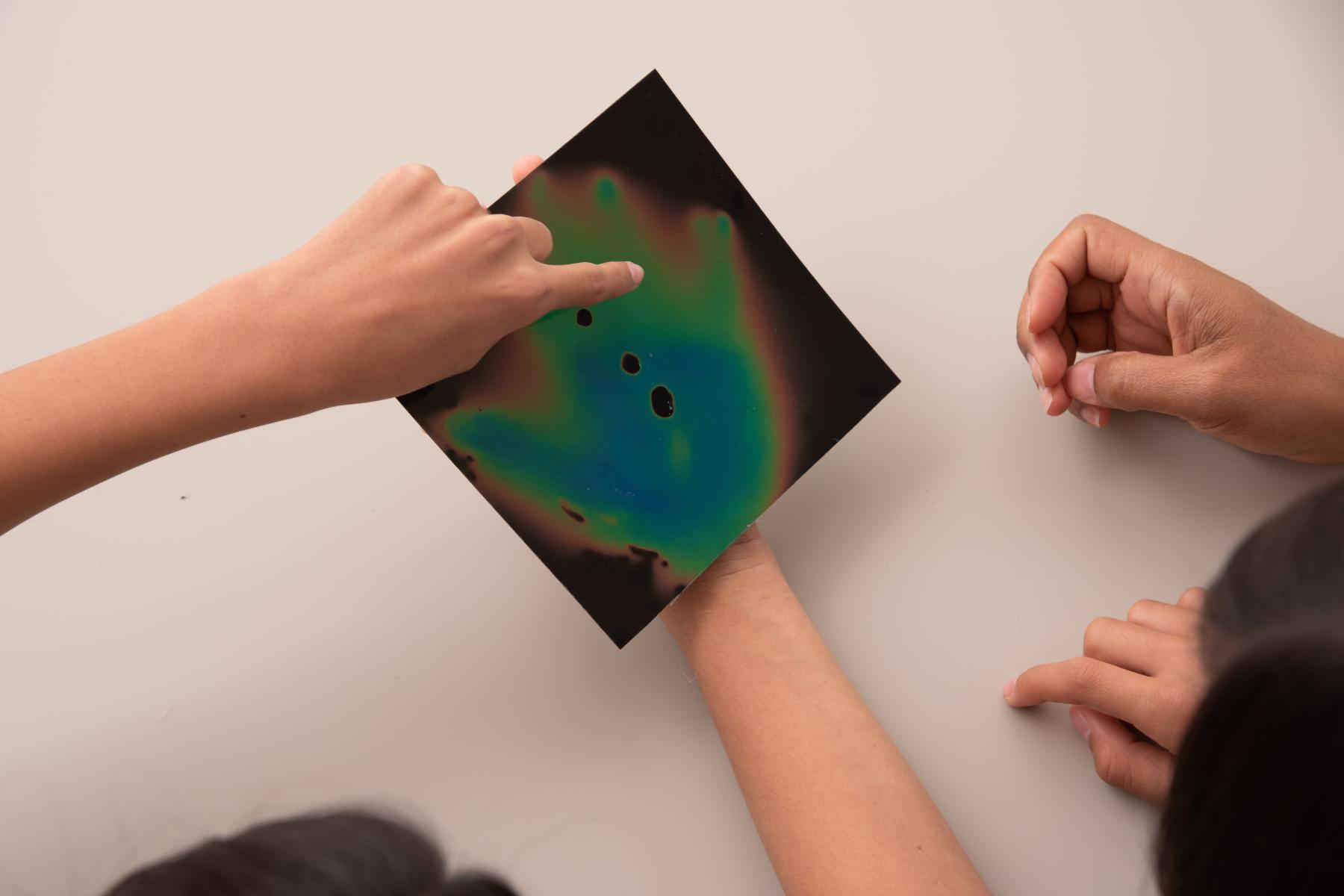 Heat sensitive film showing the outline of the hand of a learner playing with the material