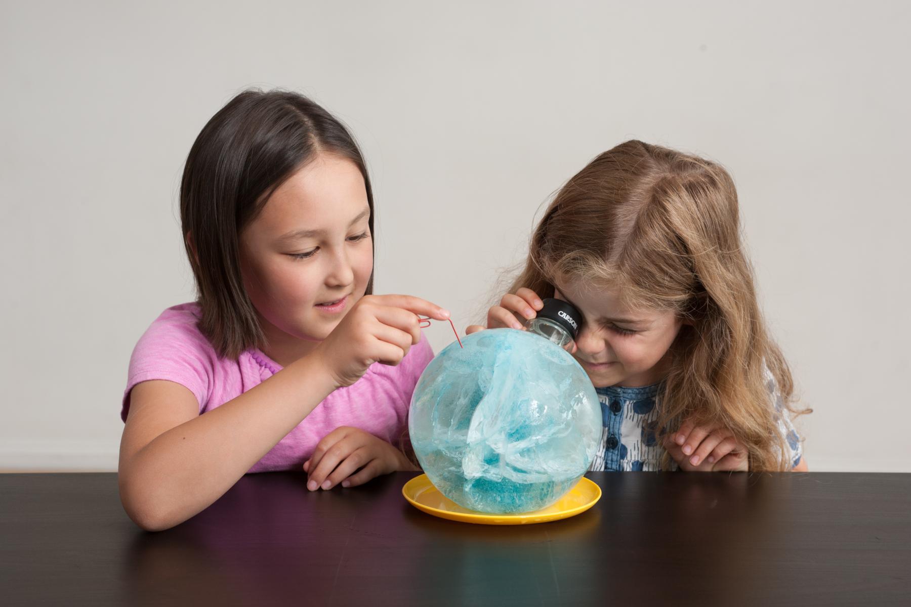 Learners examine a large sphere of ice with a magnifying glass and paperclip