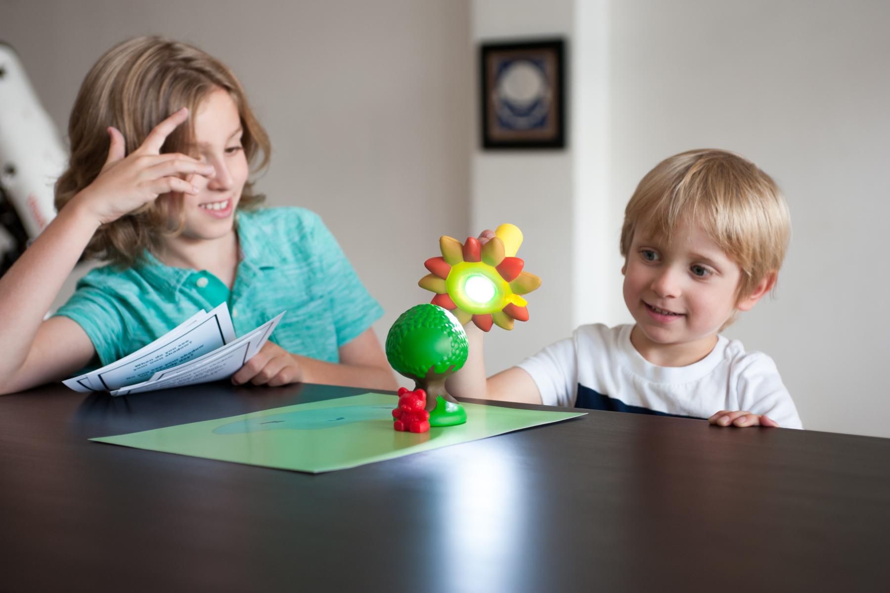 Two young learners experiment with making shadows with a toy tree, bear and a flashlight 