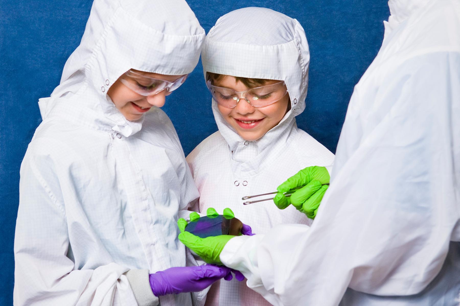 Two learners and a facilitator wear white head to toe coverall cleanroom suits with gloves and safety goggles