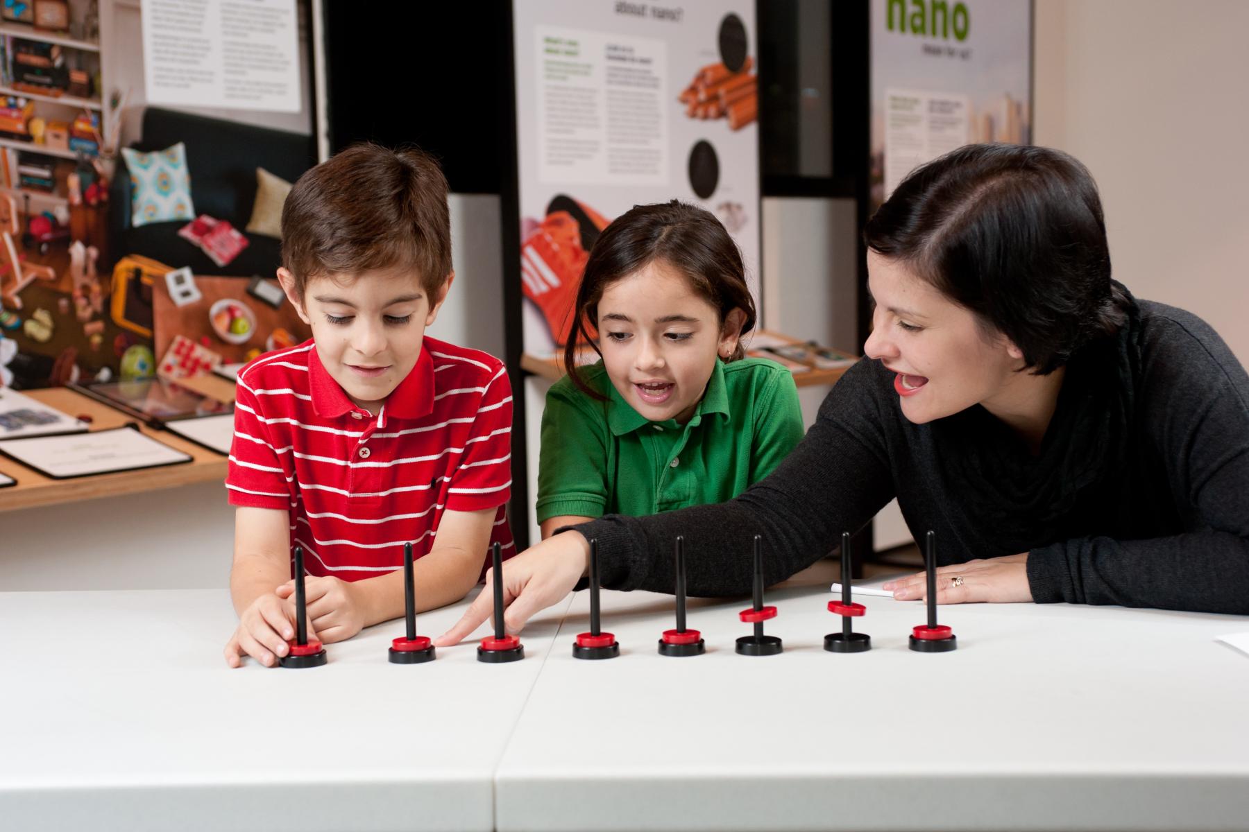 Two young learners and facilitator push down on a red magnet being repelled by a magnetic black base