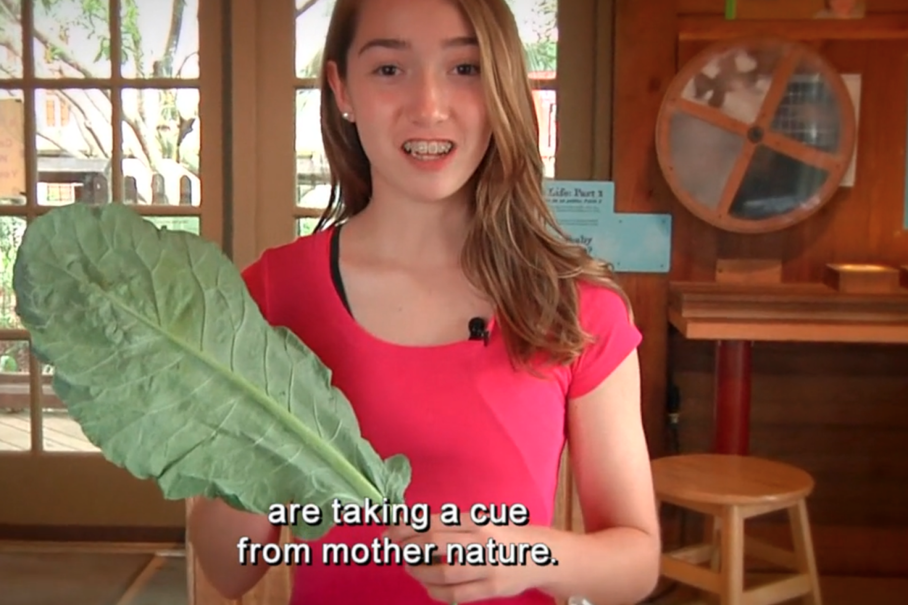 Teen girl with braces in a pink shirt holds a large kale leaf
