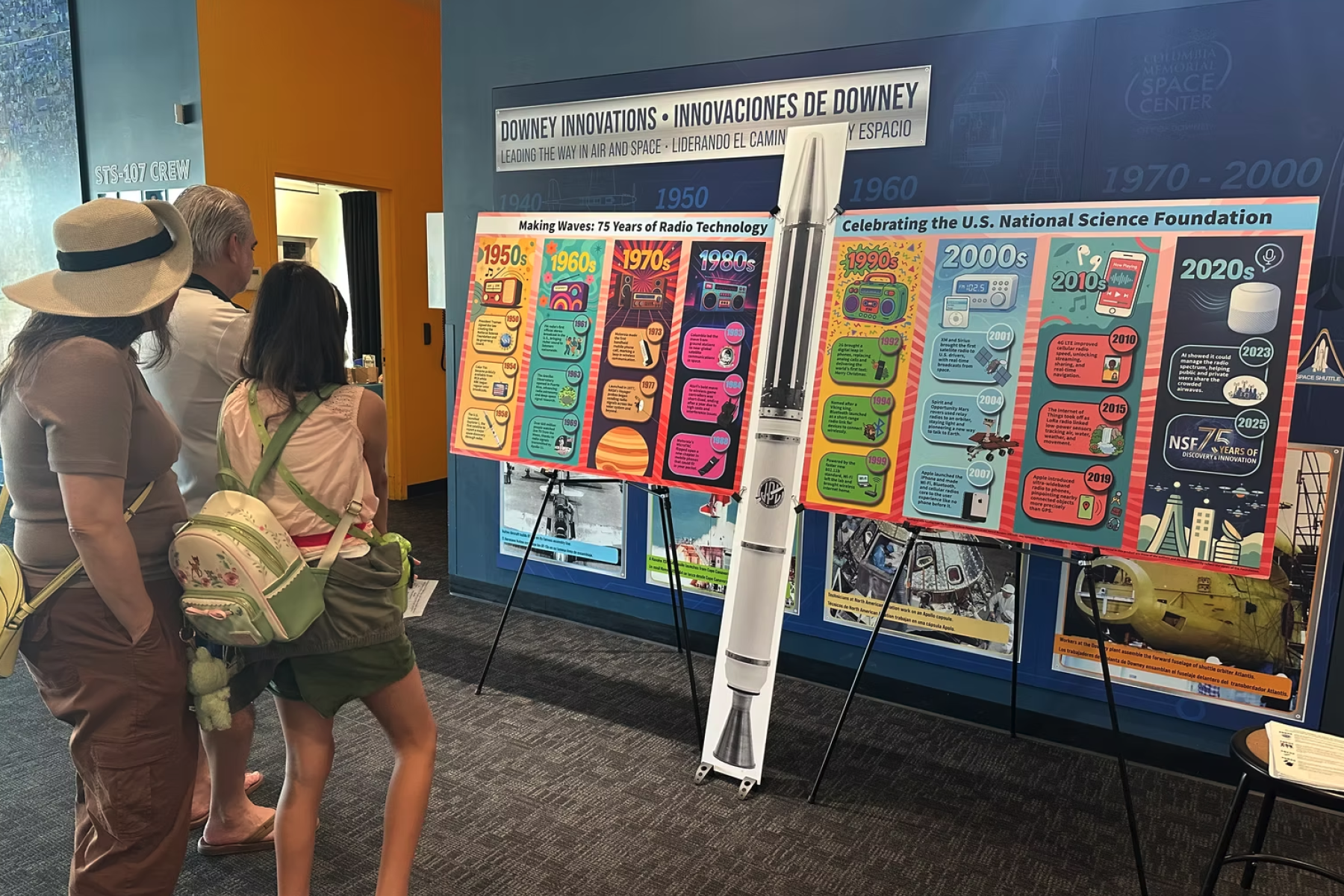 A family views a colorful, large-format radio technology timeline display at a science center exhibit.          Ask ChatGPT
