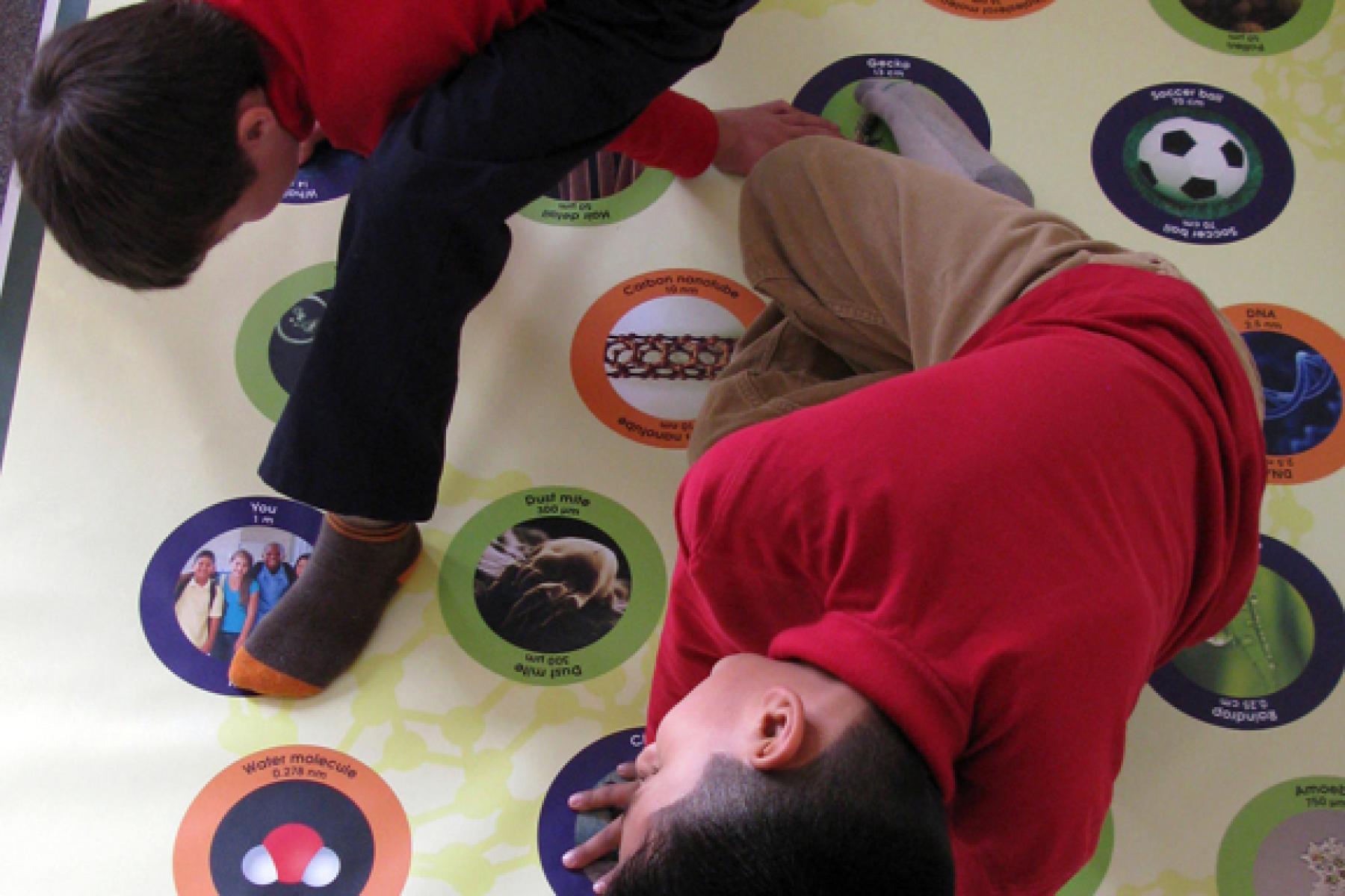 two learners stretch across a large mat that have various icons related to nanotechnology