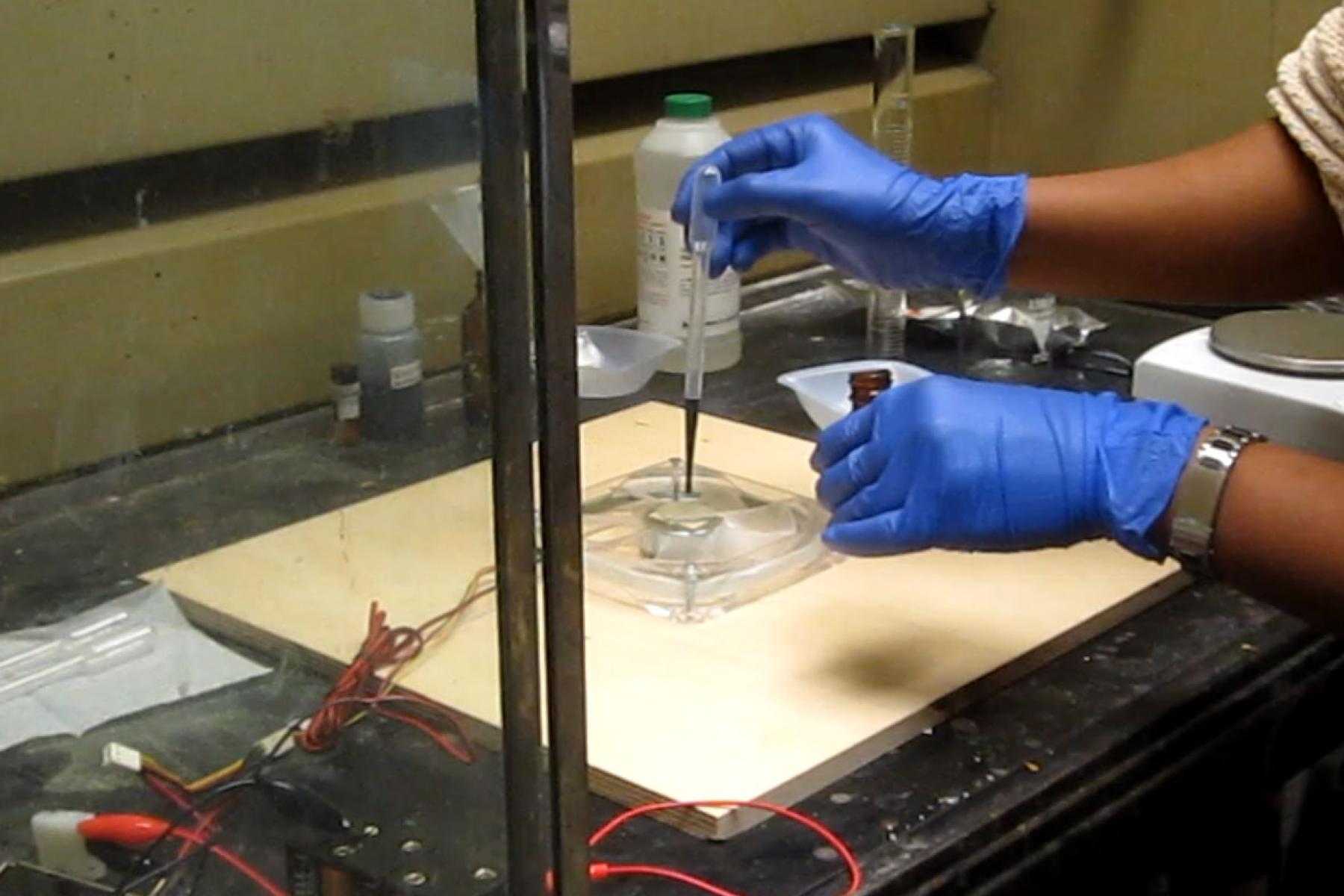 A person puts a liquid on a substrate which is on top of a DIY spin-coater. 
