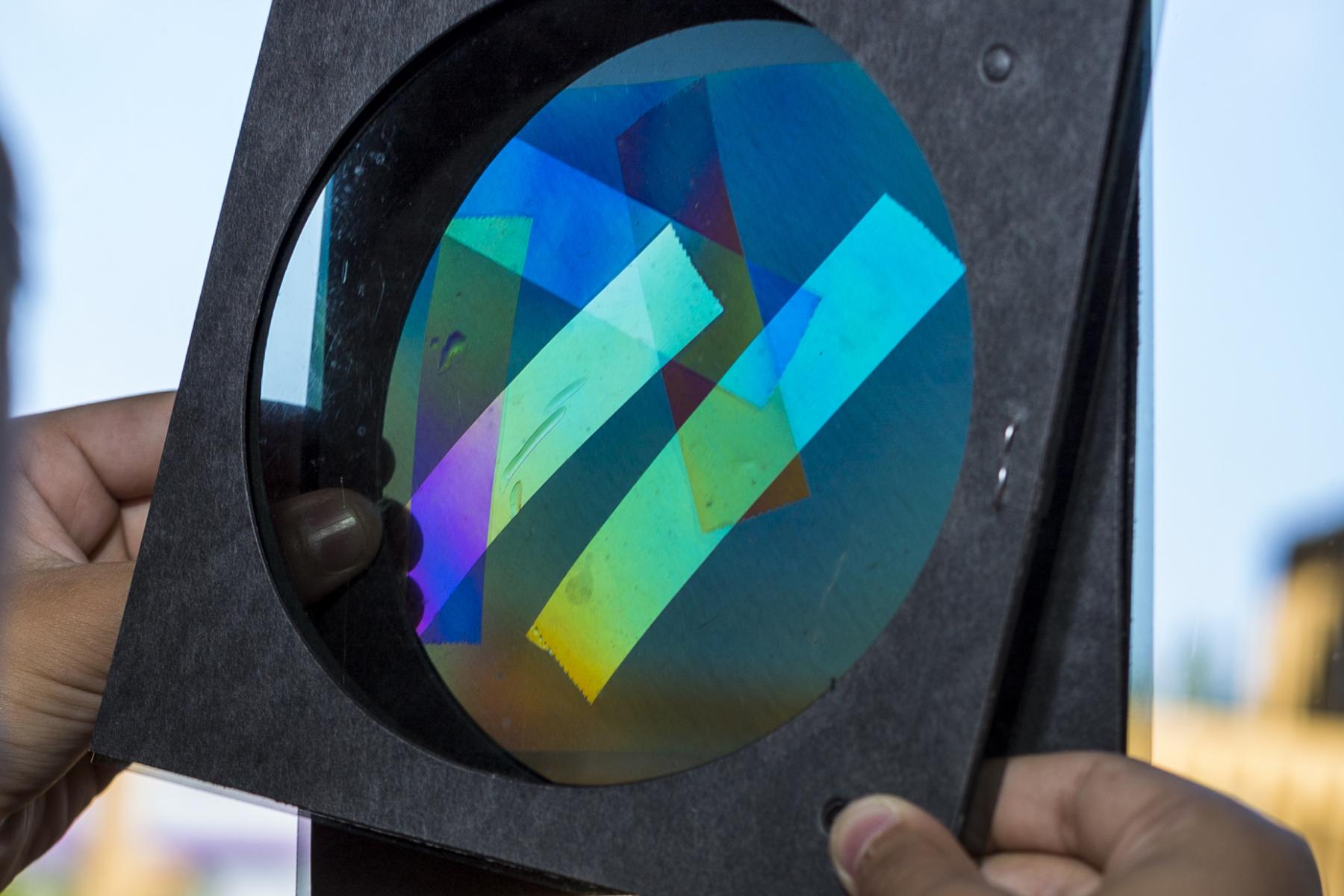 Hands holding square of polarizers and transparent tape