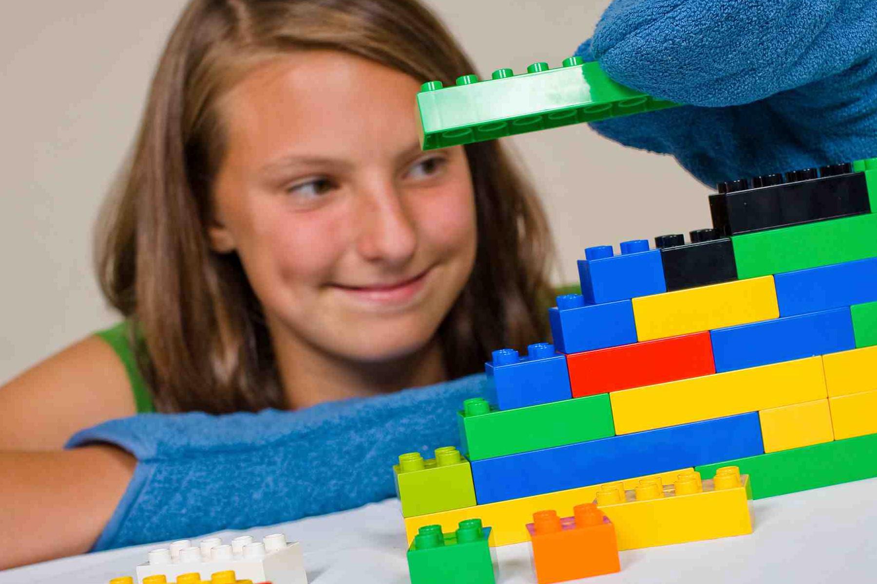 A person building a structure with Lego® while wearing mitts. 