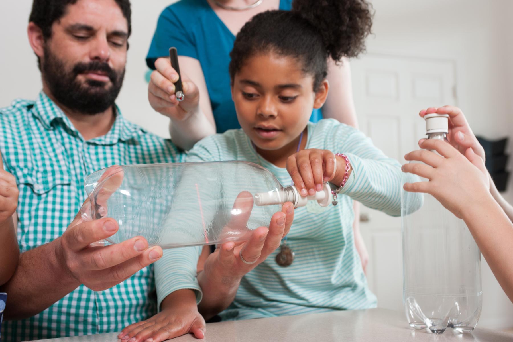 a family of learners use a laser to better see a cloud they made in a bottle