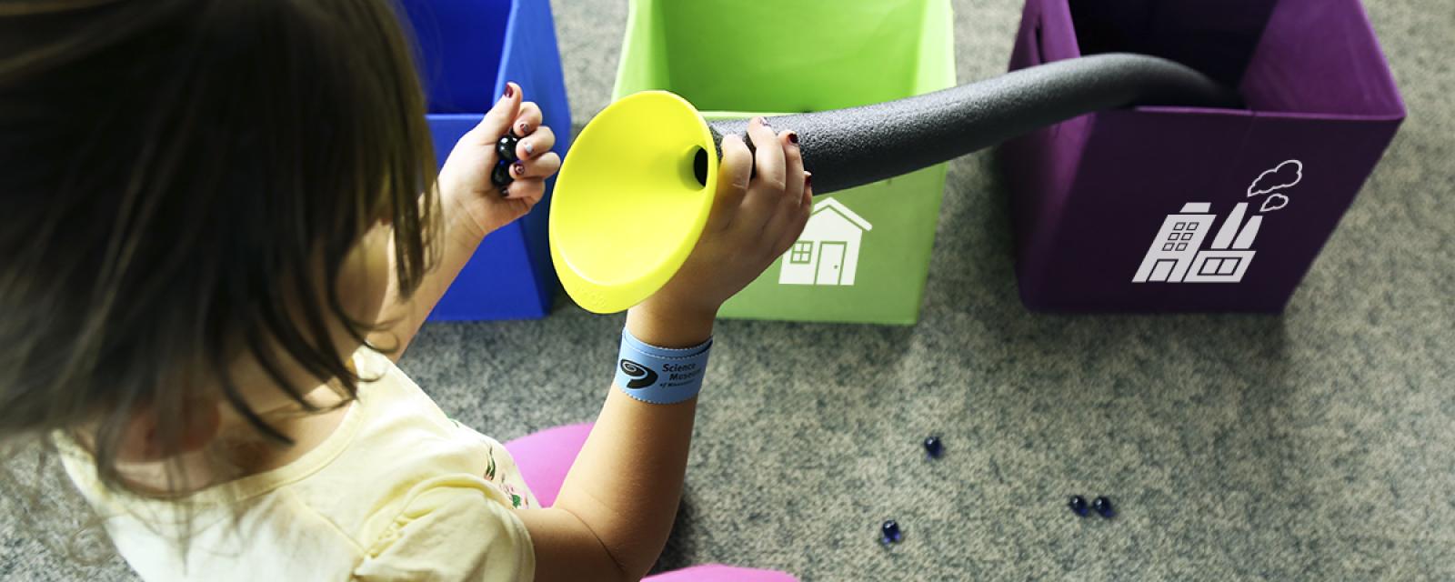 Child using putting marbles into tube with funnel in Water Roll SustainABLE kit activity