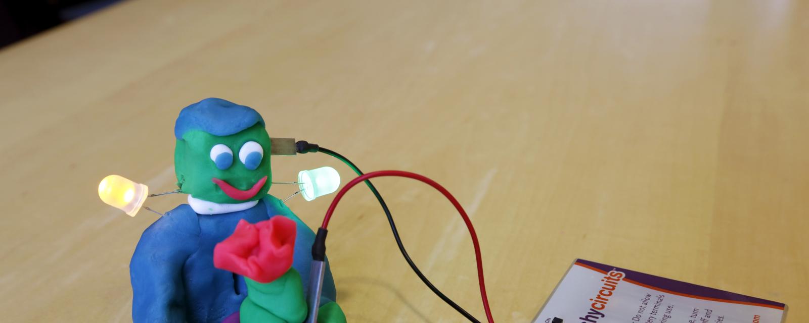 Lit up dough creature holding flower with squishy circuit battery pack and wires
