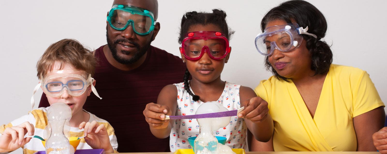 Two facilitators and two learners wearing goggles use colorful felt strips to layer bubbles upon each other